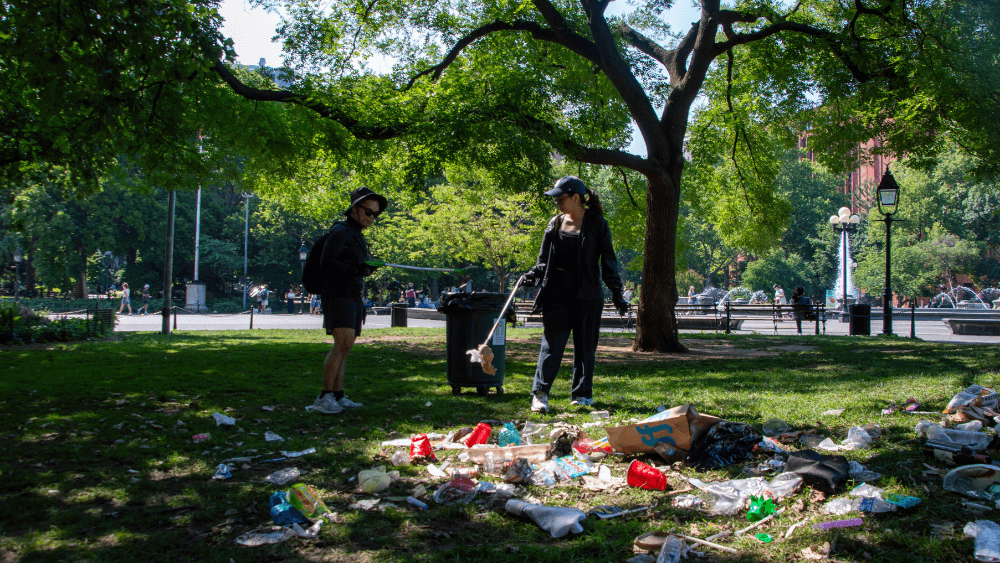 Two people clean up garbage in Washington Square Park.
