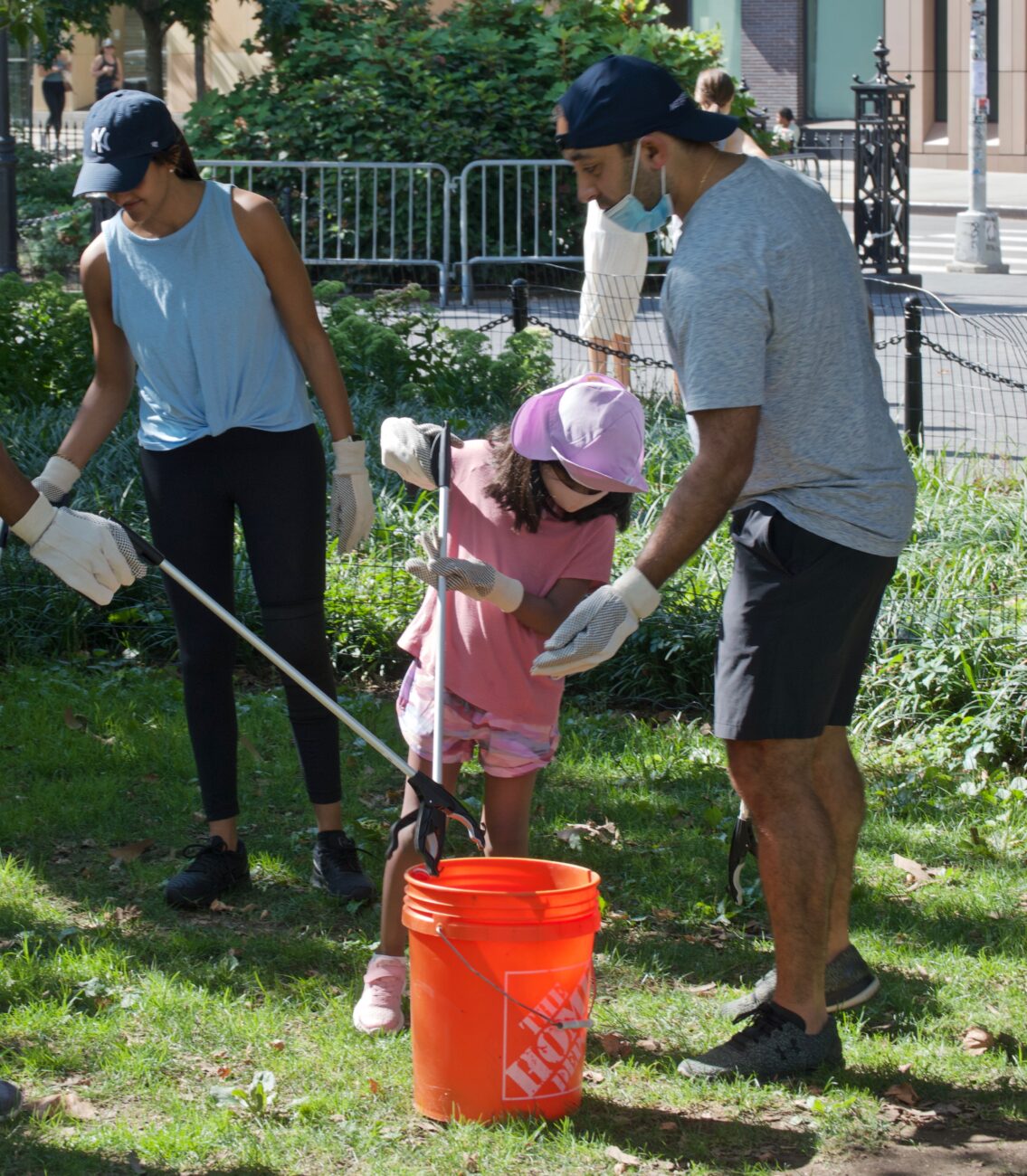 two adult volunteers and one child volunteer use tools to pick up litter in the park