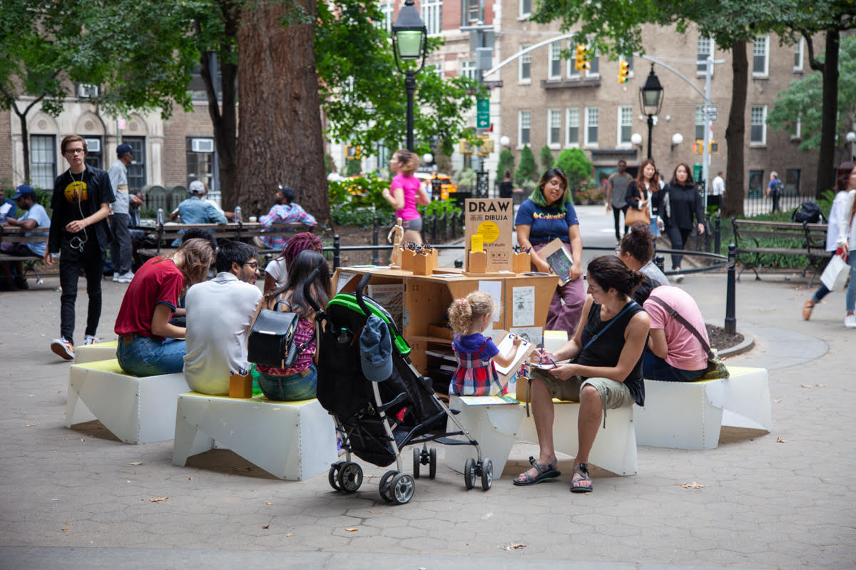 people of varying ages sit in a circle at the DrawNYC pop-up studio in the park