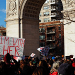 protesters under the arch hold signs with messages supporting women's rights
