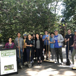 a large group of volunteers poses with cleaning tools in the park at a monthly clean up event