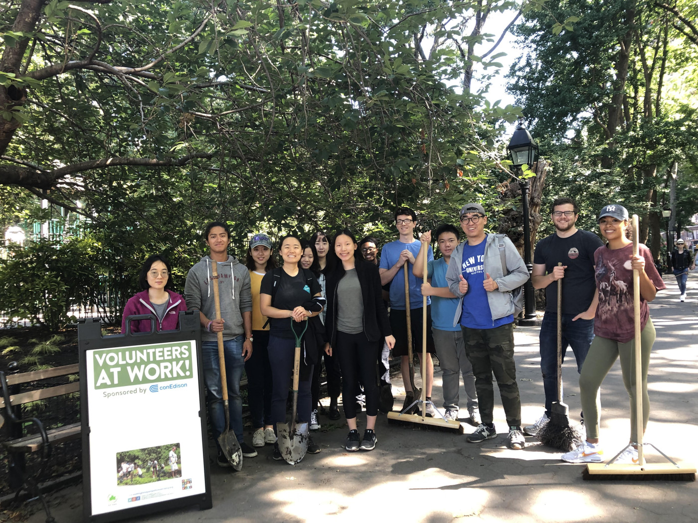a large group of volunteers poses with cleaning tools in the park at a monthly clean up event