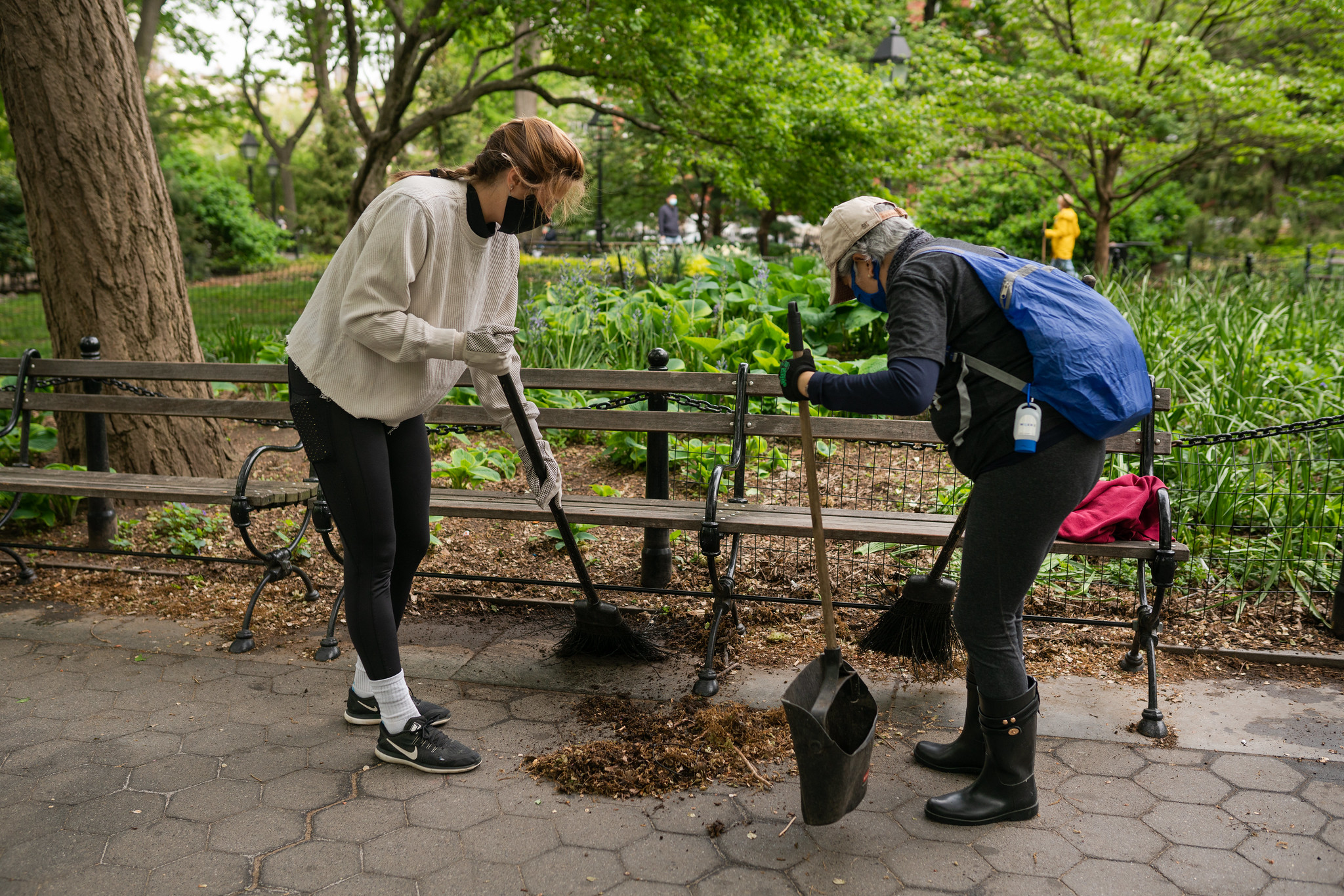 two volunteers sweep dirt off a paved pathway in the park