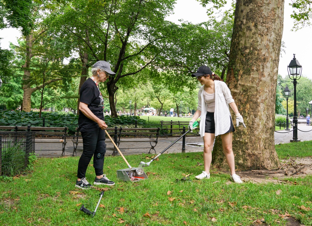 two volunteers clean up litter in the grass with cleaning tools