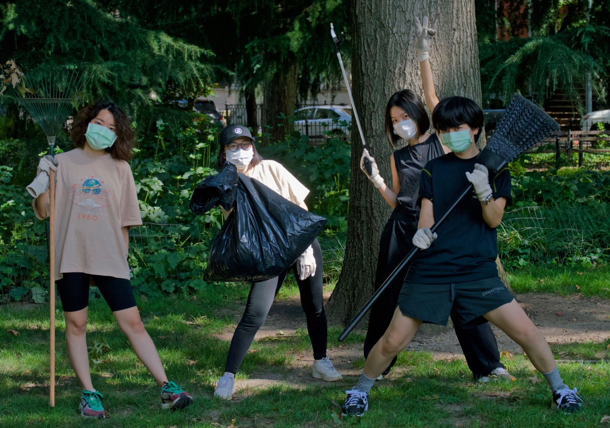 four volunteers pose for the camera while wearing protective masks, gloves, and holding cleaning tools in the park