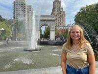 Volunteer Programs Manager, Maggie, smiles and stands in front of the fountain with arch in the background