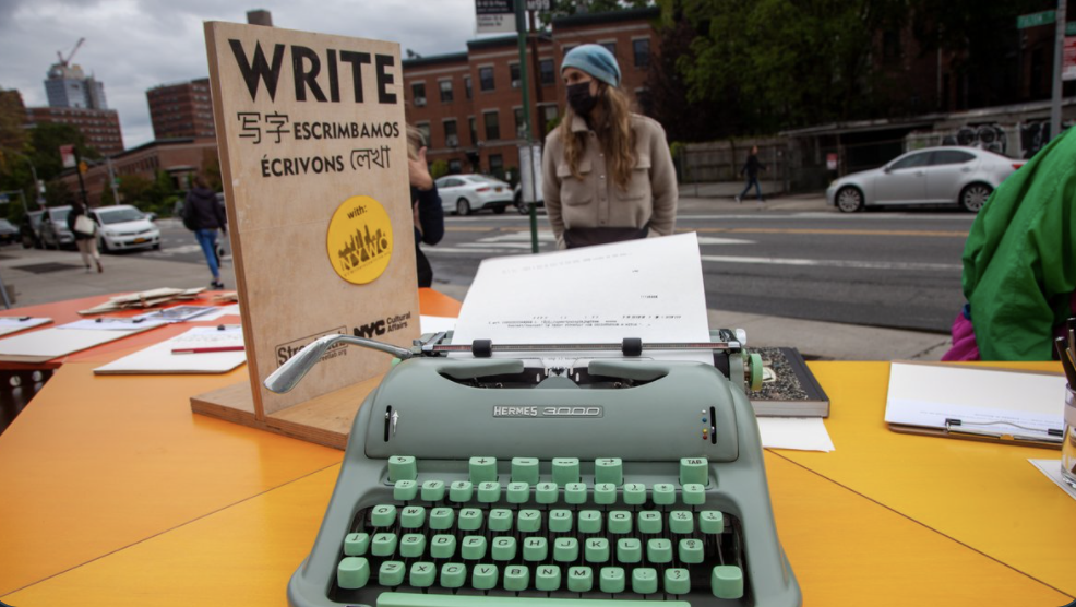 photo taken from the perspective of someone sitting at a table outside with a green typewriter during a WRITE NYC event