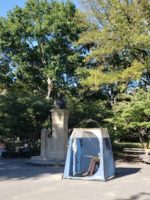 someone sits in a tent in front of Holley monument