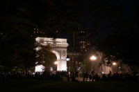 crowded park at night, lights illuminate the park and the arch