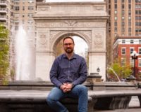 Park Administrator Will sits in front of the fountain and arch smiling for the camera