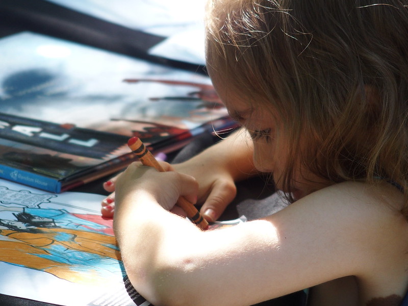 a child uses an orange crayon to color in a coloring page