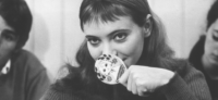 black and white still from the 1964 film Bande à Part, woman looks past the camera smiling and partially covering her mouth with a decorated paddle