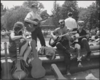 black and white photo of four people playing guitars and singing while sitting on the fountain