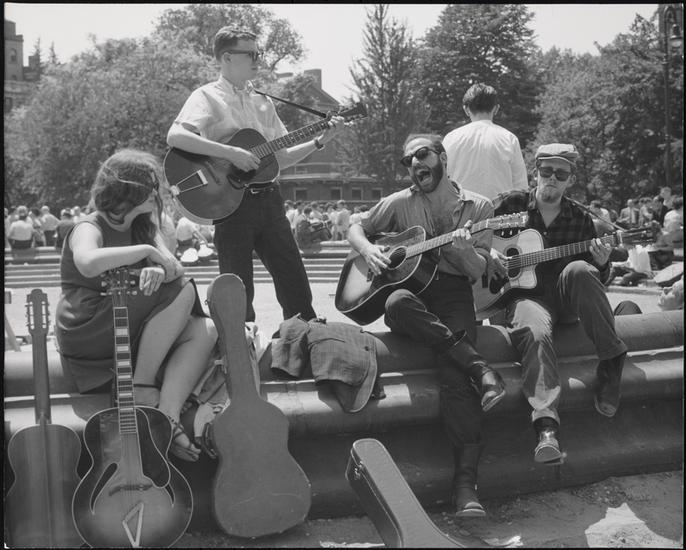 black and white photo of four people playing guitars and singing while sitting on the fountain