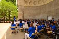 orchestra and conductor performing in the park wearing matching blue shirts