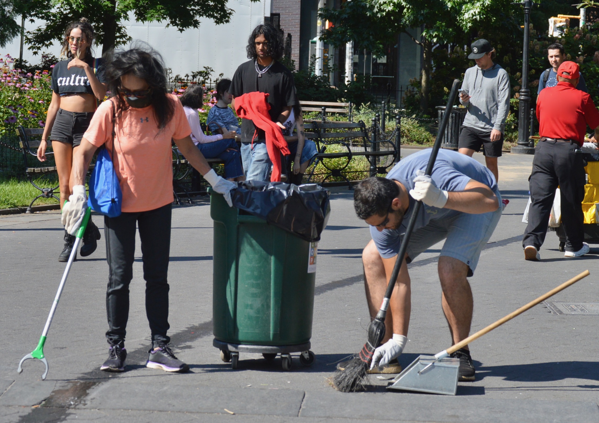 two volunteers use tools to pick up litter while people walk past them