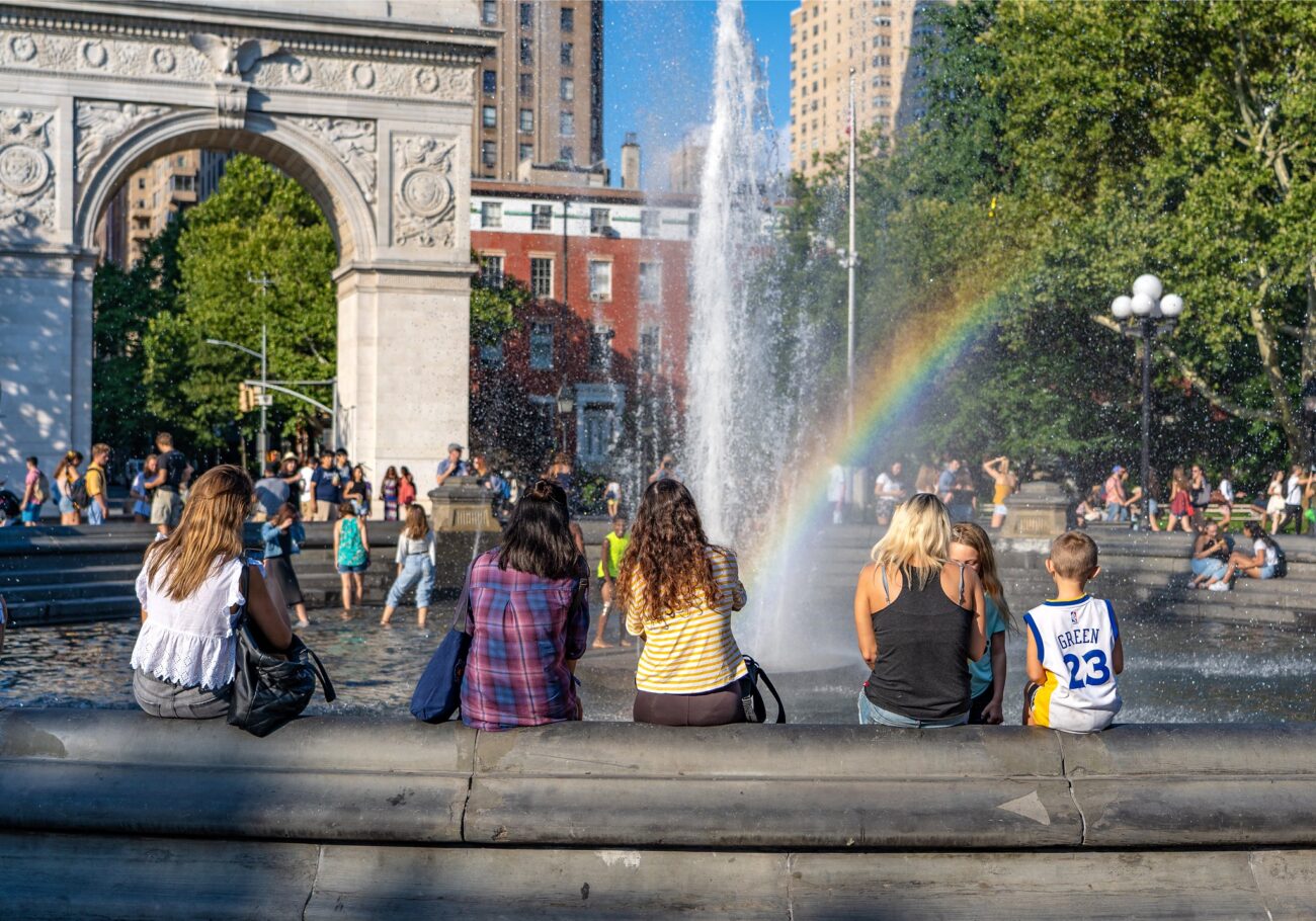 a rainbow appears over the WSP fountain, people sit on the rim with their backs to the camera