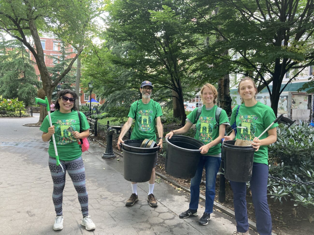four volunteers in green t-shirts pose smiling with gardening tools