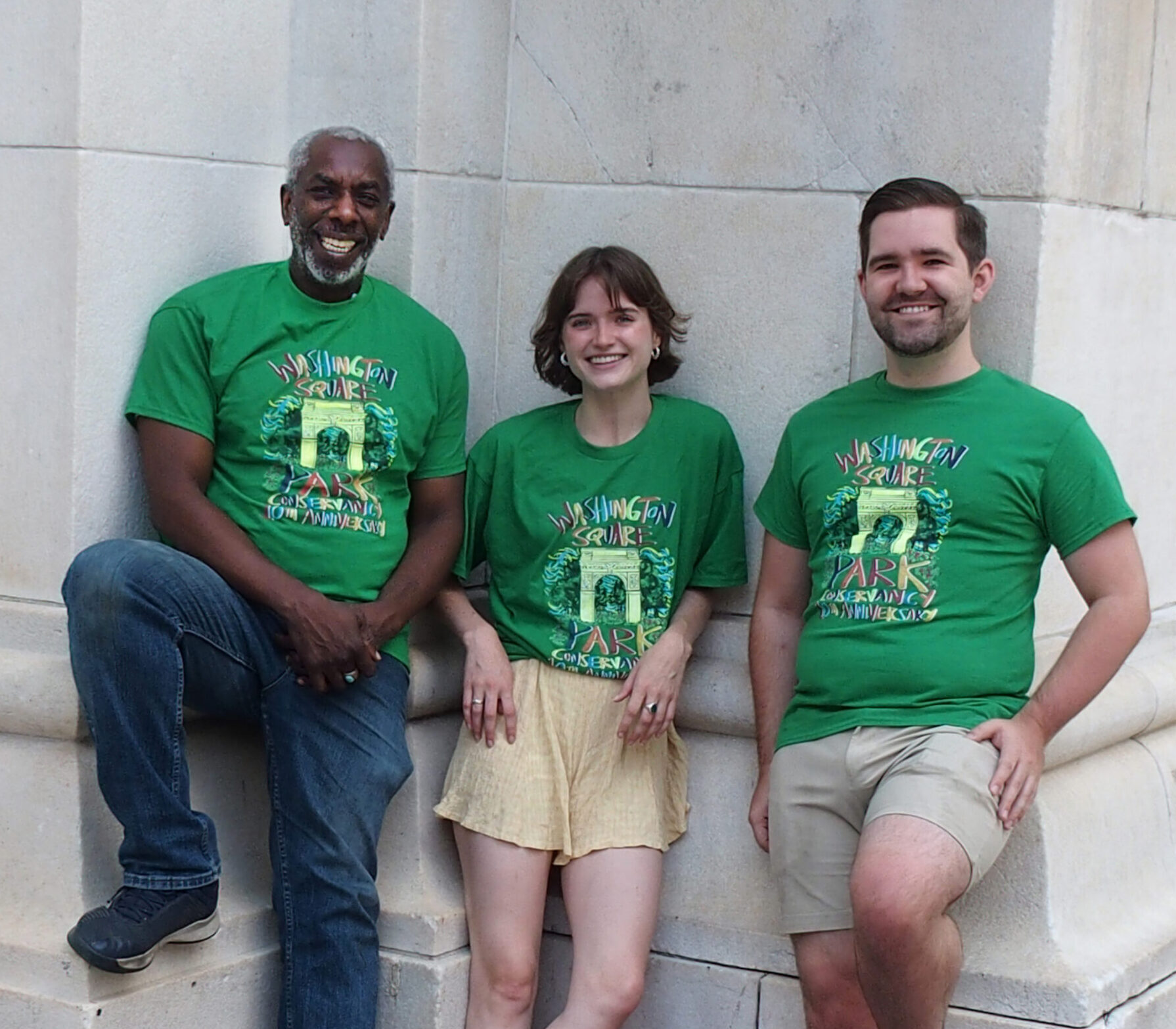 three volunteers wearing green washington square park shirts posing and smiling