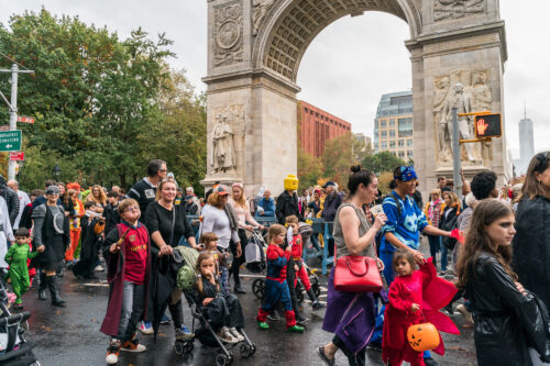children and families in Halloween costumes march in the NYU parade in front of the Arch